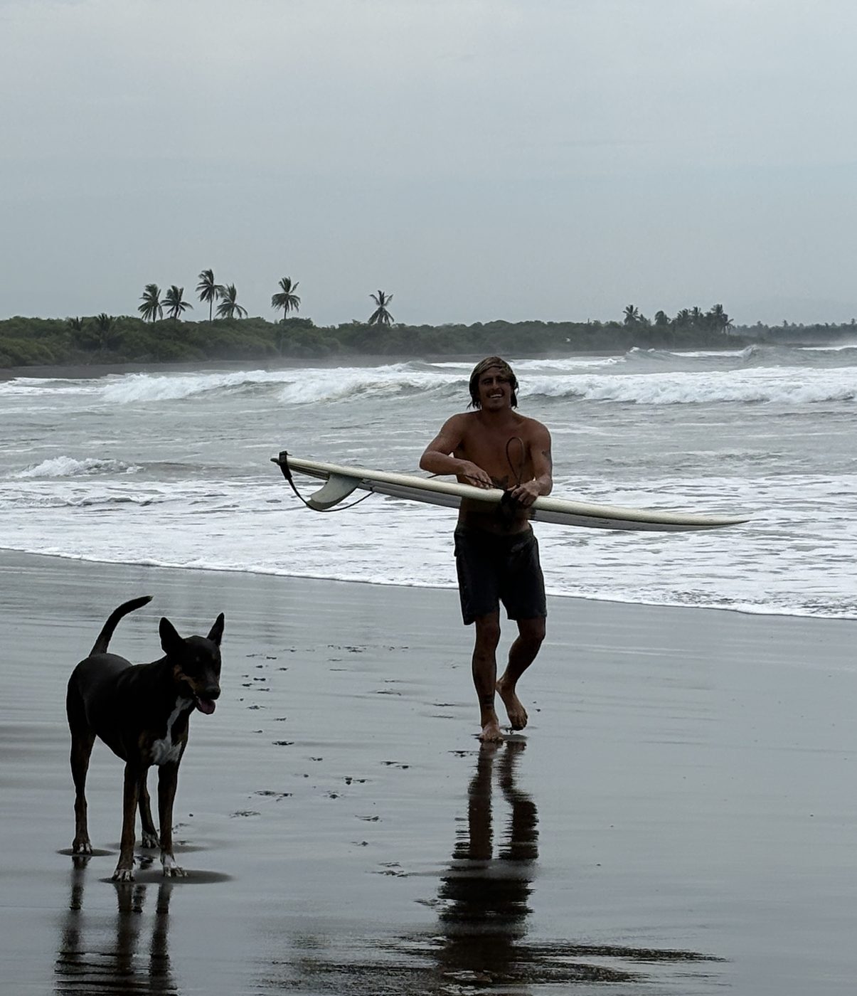 Carlos walking out of the surf with his board and his dog