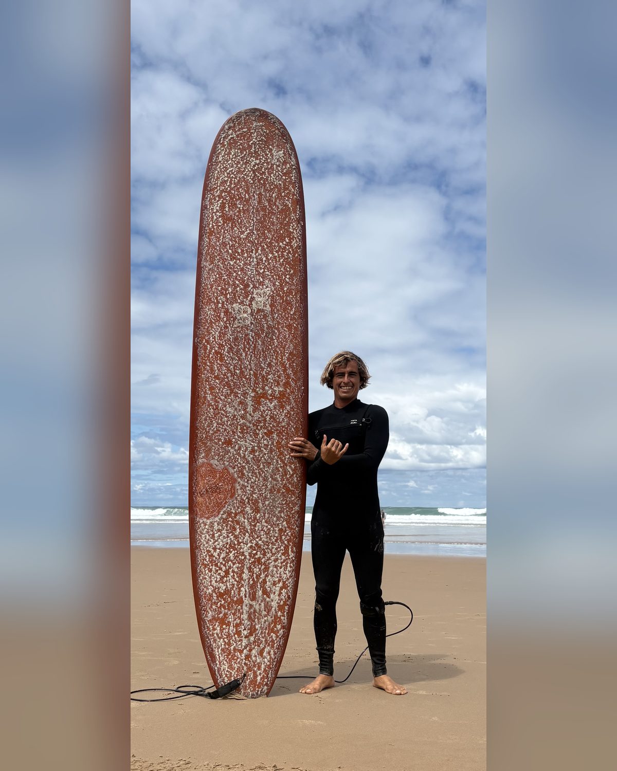 Carlos standing next to his longboard on the beach