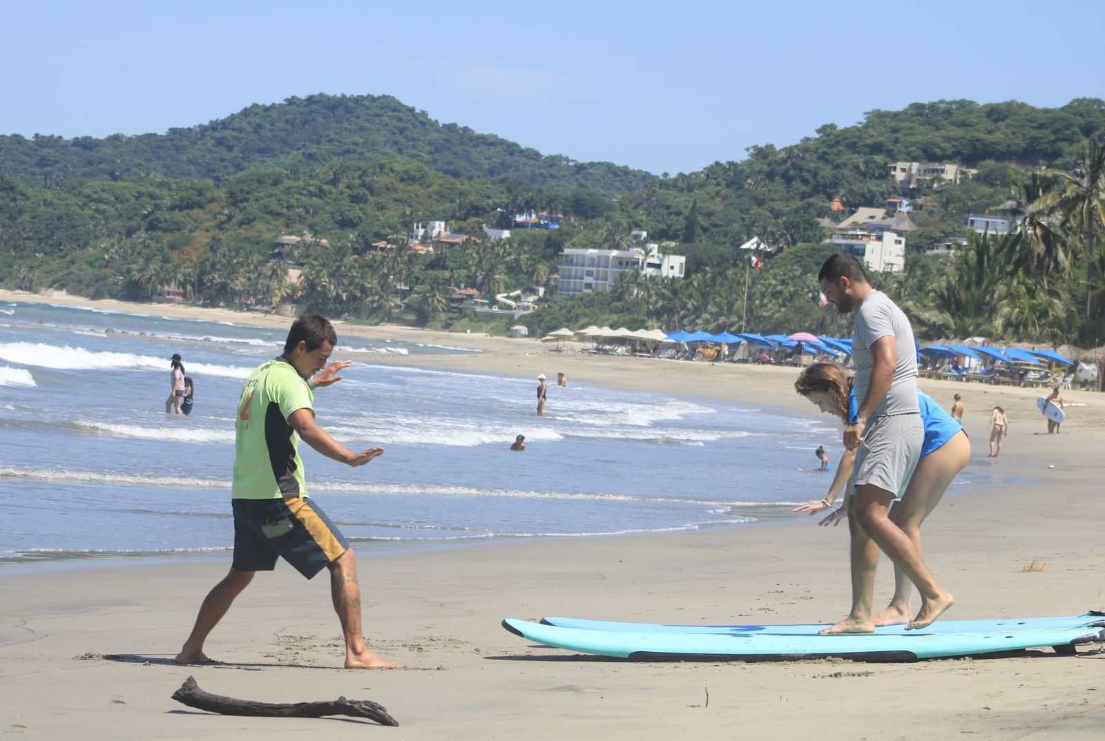 Carlos showing stance on the sand next to two students on boards